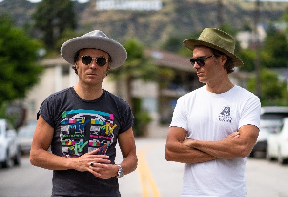 EC Twins wearing hats and sunglasses on a Los Angeles street with the Hollywood sign in the background